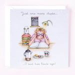 A greeting card with an illustration of a women reading a book, accompanied by a coffee cup, a stack of books, and a clock, with a caption that reads 'Just one more chapter.