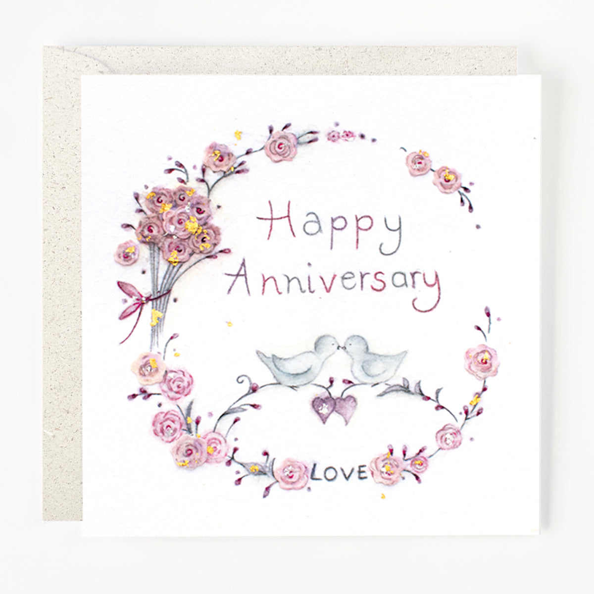 A greeting card with a floral wreath design and the text 'Happy Anniversary' in the center. There are two birds perched on hearts.