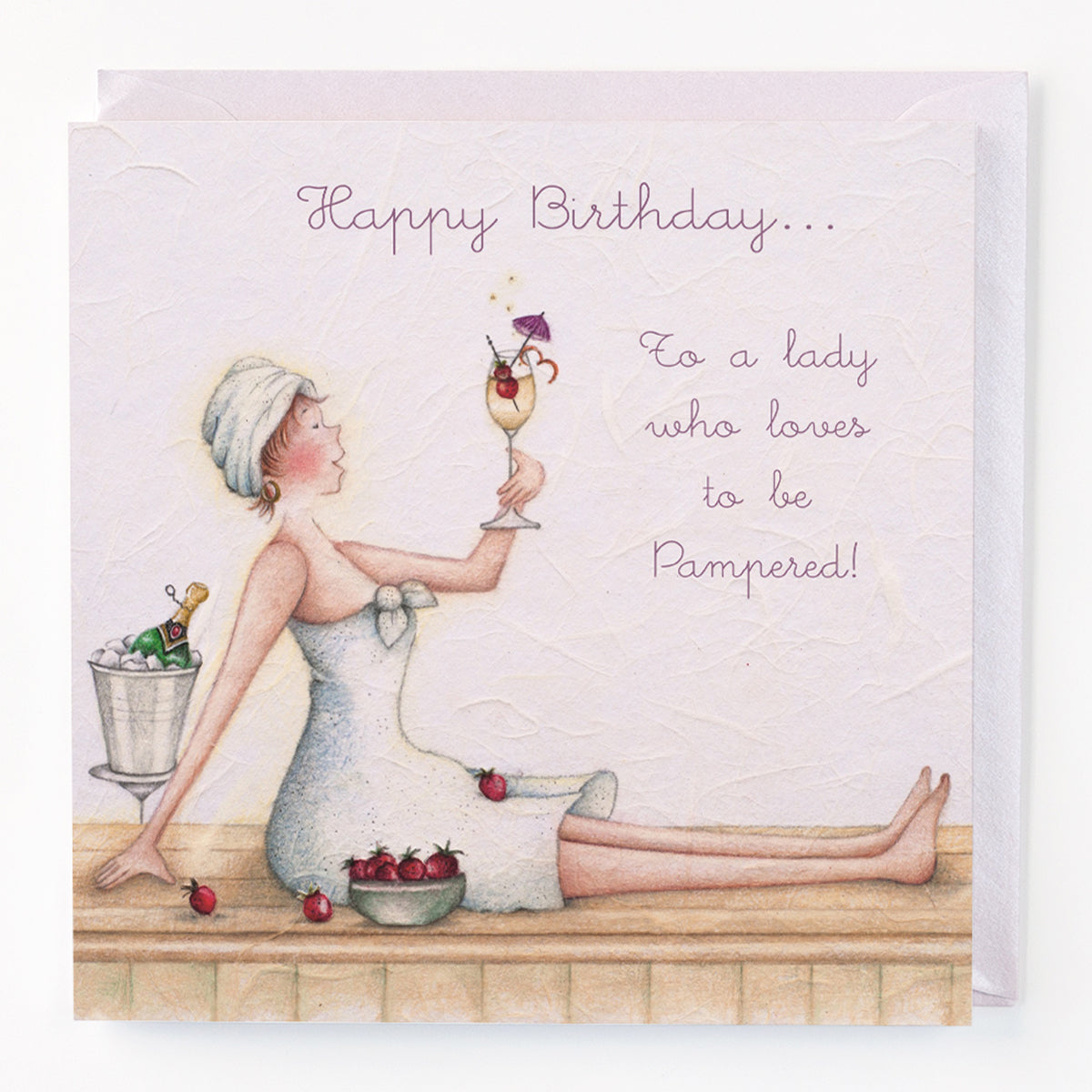 A greeting card with a hand drawn illustration of a woman in a bathrobe sitting and holding a champagne glass, with a basket of fruits beside her. The card has 'Happy Birthday to a lady who loves to be Pampered!'.
