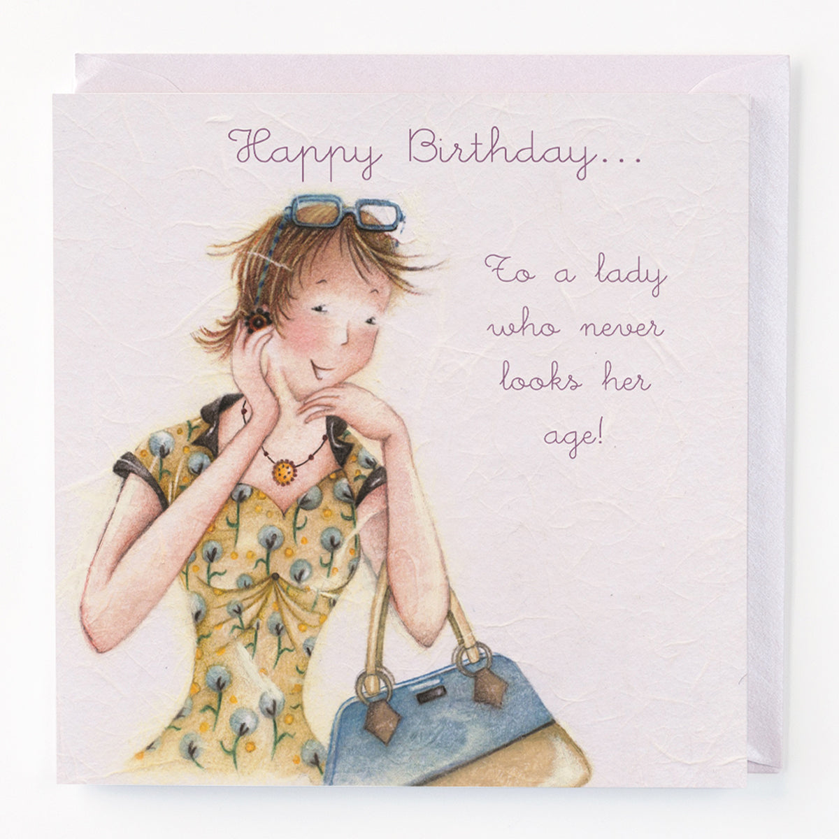 A birthday card with an illustration of a woman in a yellow floral dress, holding a blue handbag, with the text 'Happy Birthday to a lady who never looks her age!'